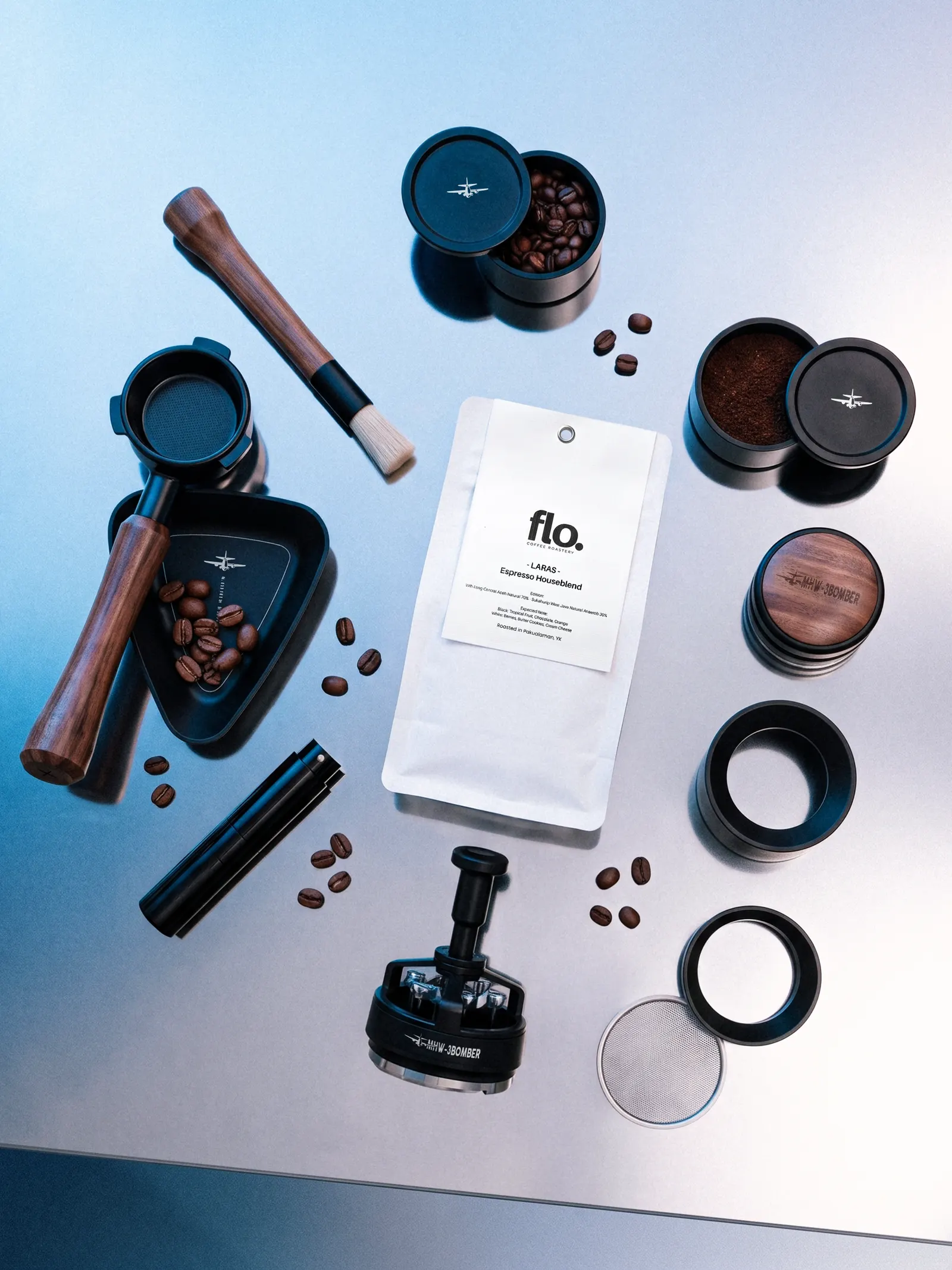 Espresso brewing tools, a bottomless portafilter and a bag of Laras Espresso Houseblend laid out on a steel-blue surface.