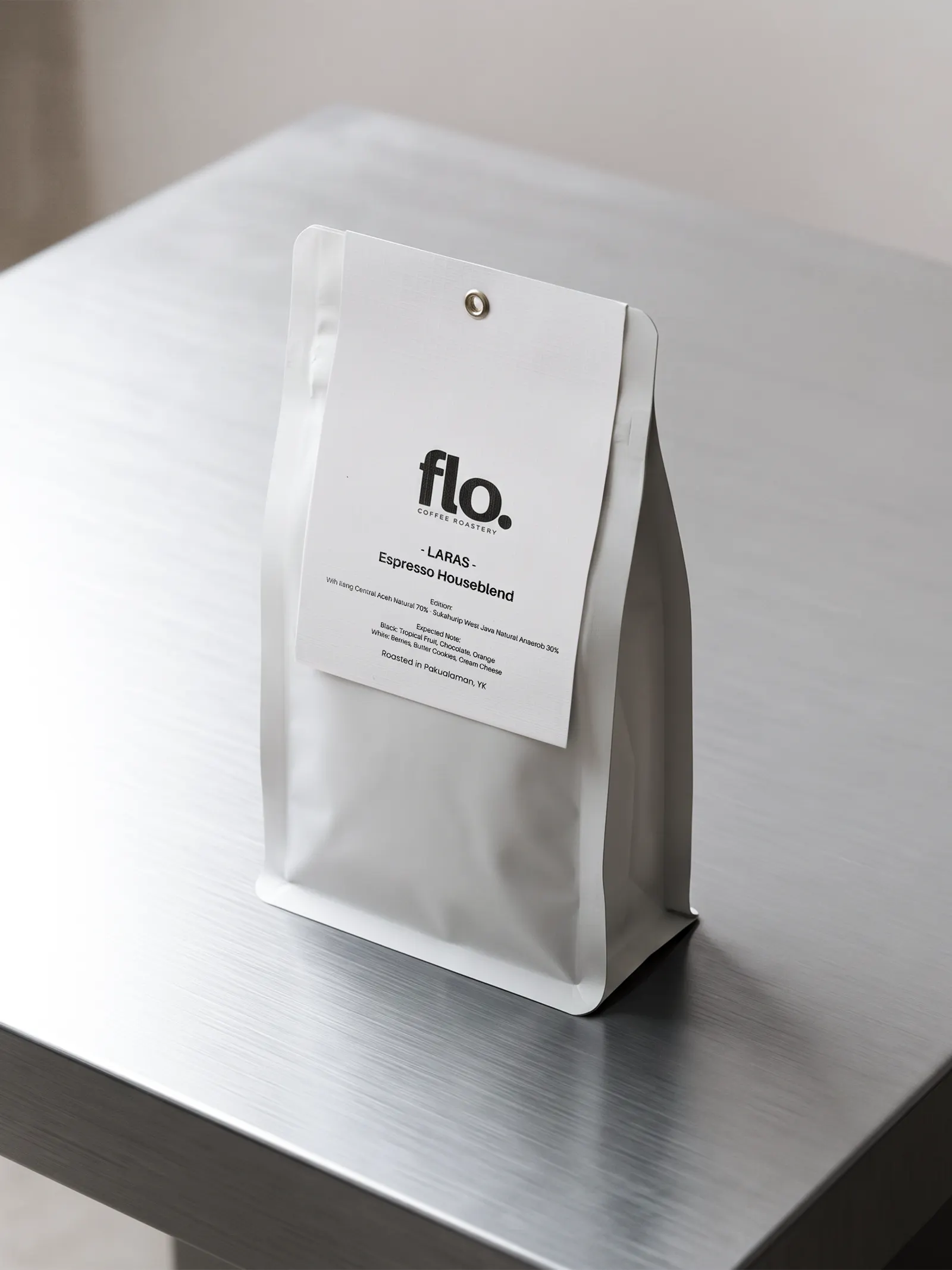 A white flo. Coffee Roastery bag of Laras Espresso Houseblend standing on a brushed steel table.